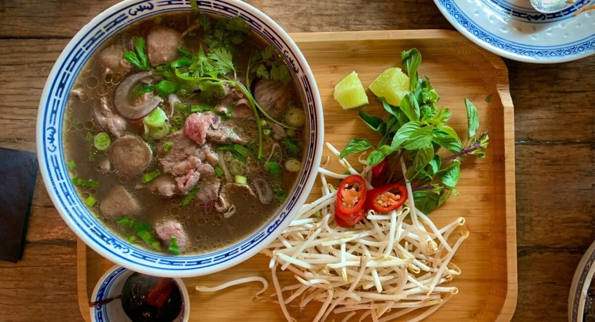 Enjoy this vibrant Vietnamese pho served with fresh herbs and spices on a wooden tray.